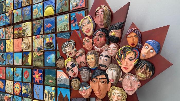 A maple leaf with faces made out of clay as part of a mural wall