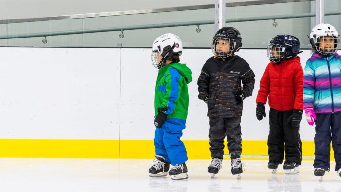 Four children wearing protective gear standing in an ice rink.