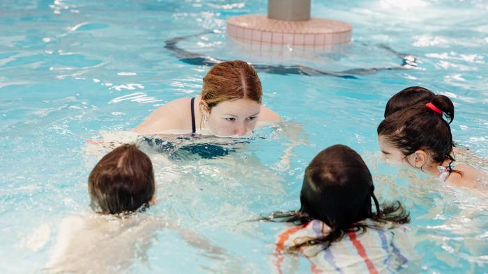 Swimming lesson instructor and three students in pool
