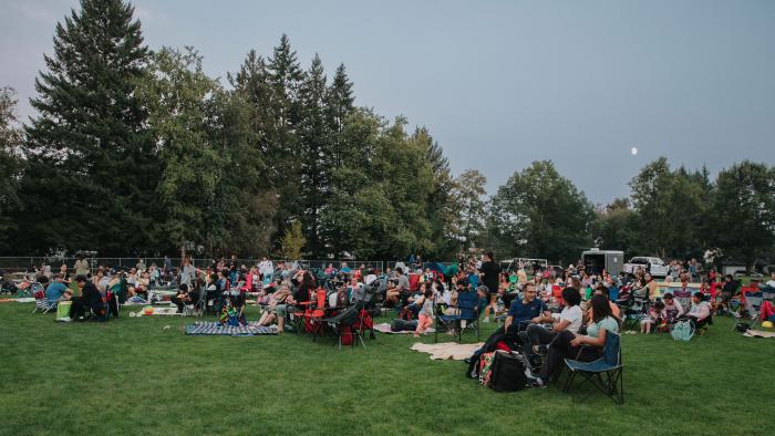 People sitting in Evergreen Park with lawn chairs and blankets at an outdoor movie event