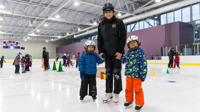 Skating instructor holding hands with two children on indoor ice
