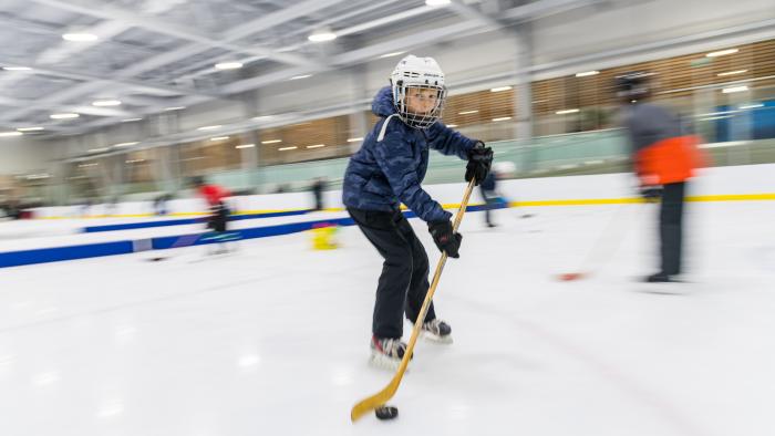 Child shooting a hockey puck on the ice at an indoor arena