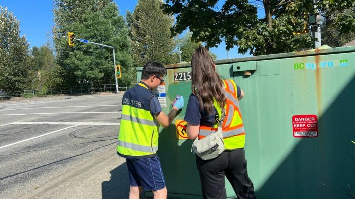 Two volunteers removing graffiti from a utility box