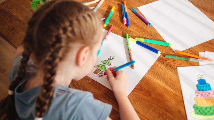 Child drawing a Christmas tree on a piece of paper with coloured pens around