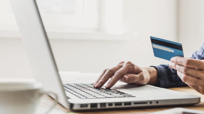 Person holding a credit card while typing on a laptop to make an online payment