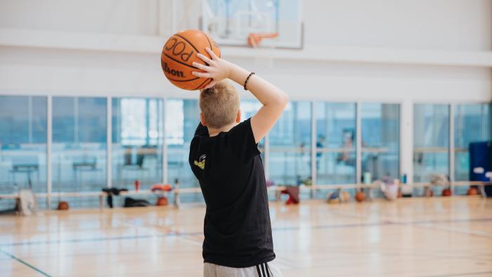 Youth shooting a basketball inside rec centre gymnasium