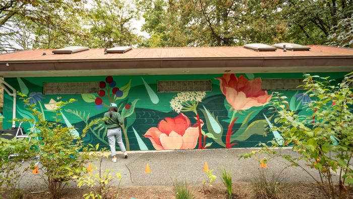 Person standing in front of floral art mural on building at Lions Park