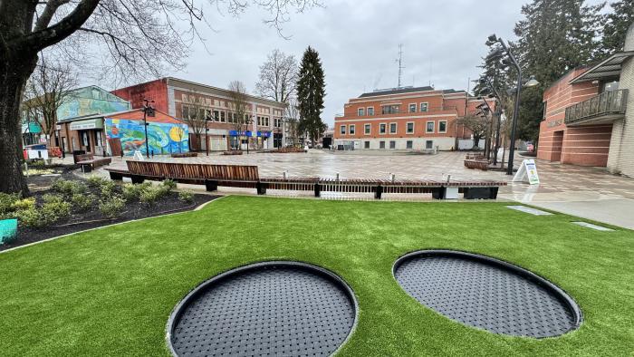 Photo of Leigh Square with green grass, two in-ground trampolines, open concept space with City Hall in background
