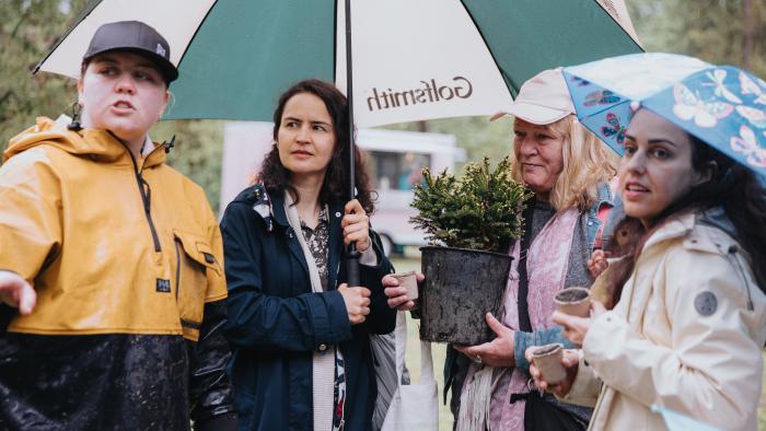 People standing under an umbrella with one person holding a tree
