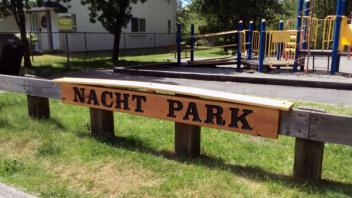 Nacht Park signage. The sign is wooden with dark lettering. The sign is on a wooden barrier.