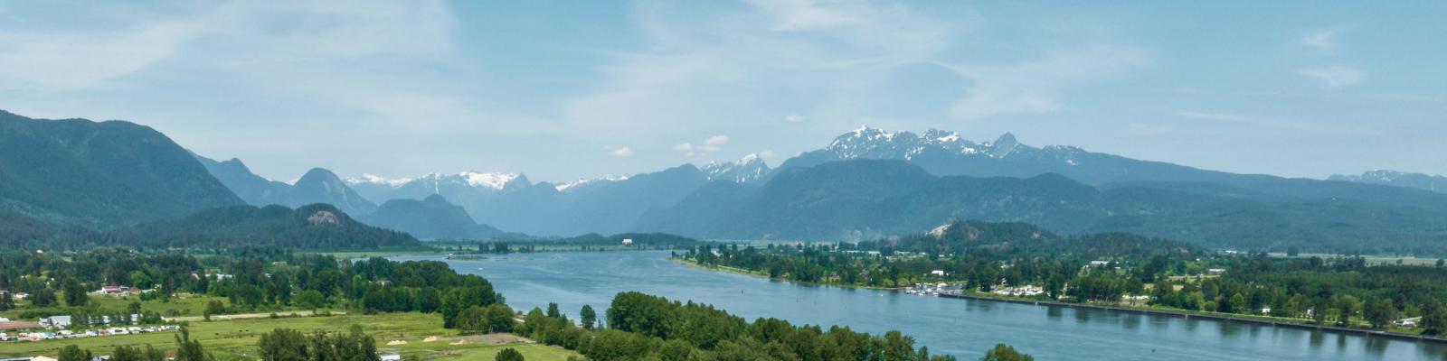 A view of a river with trees on either side and moutains in the background