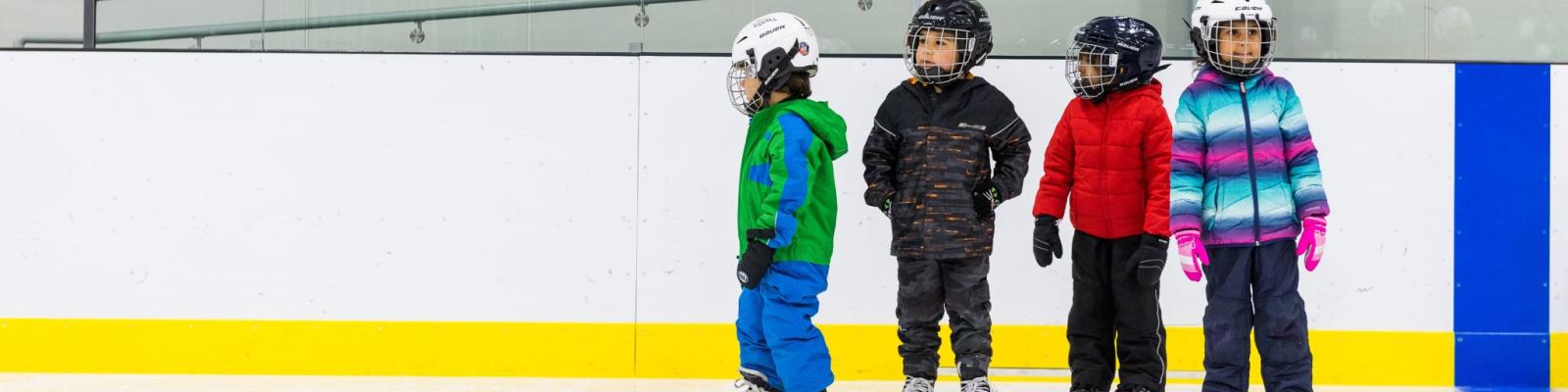 Four children wearing protective gear standing in an ice rink.