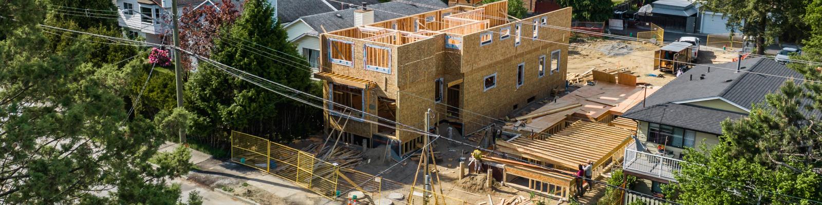 Wooden building in mid construction. The structure is is on a developed plot of land.