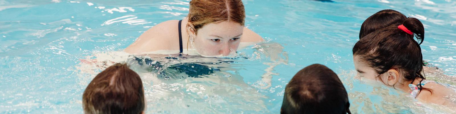 Swimming lesson instructor and three students in pool