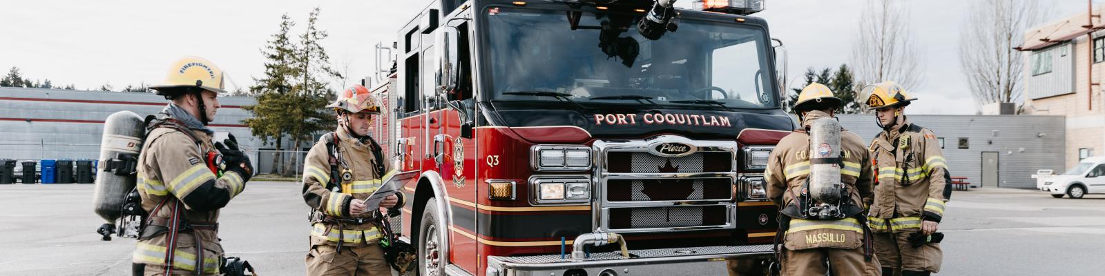 Four firefighters around a fire truck