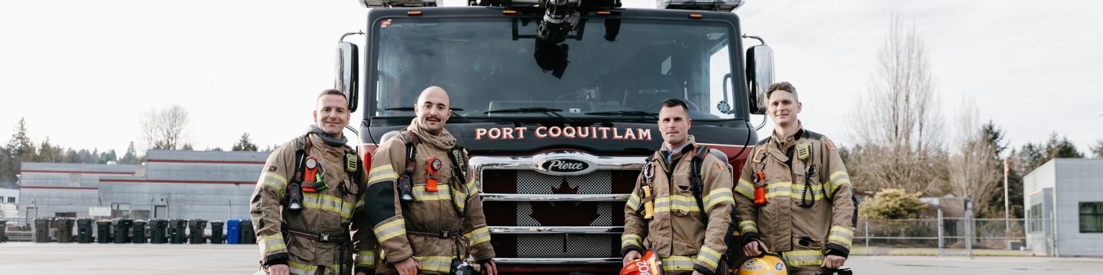 Four firefighters standing in front of a fire truck