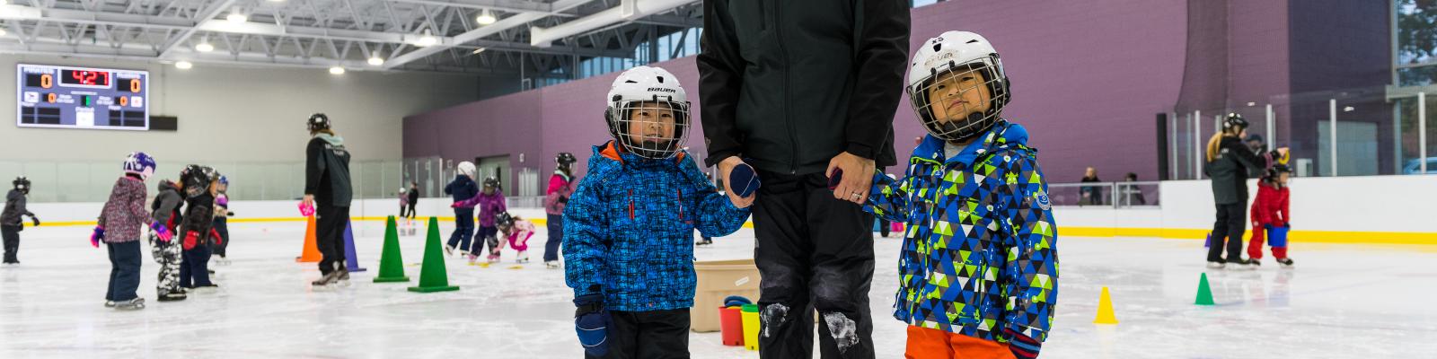Skating instructor holding hands with two children on indoor ice