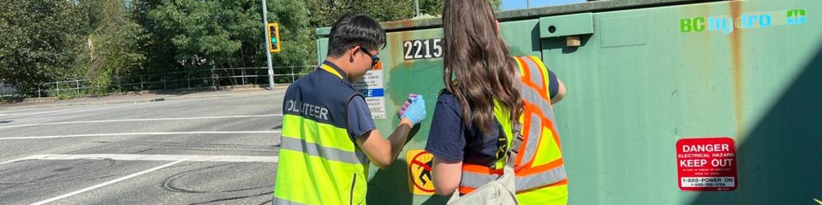 Two volunteers removing graffiti from a utility box