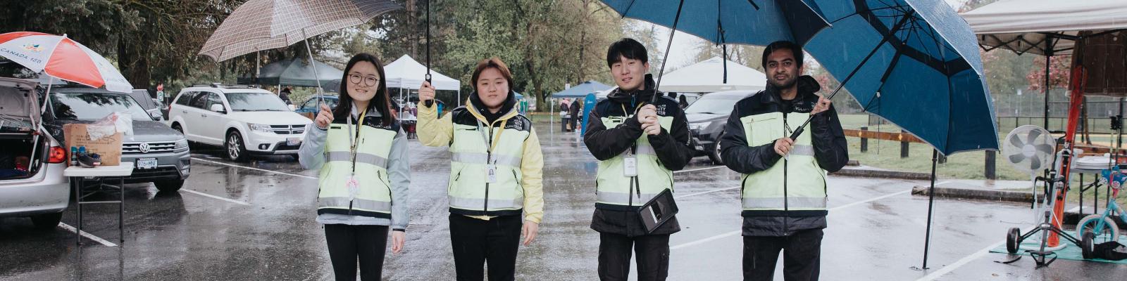 Four community police volunteering on a patrol standing under umbrellas