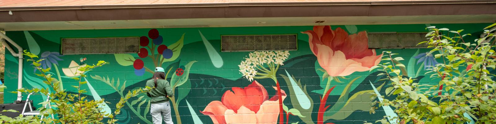 Person standing in front of floral art mural on building at Lions Park