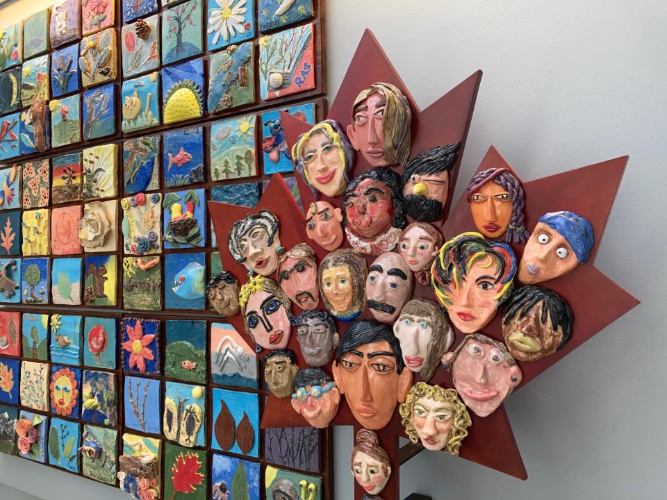 A maple leaf with faces made out of clay as part of a mural wall