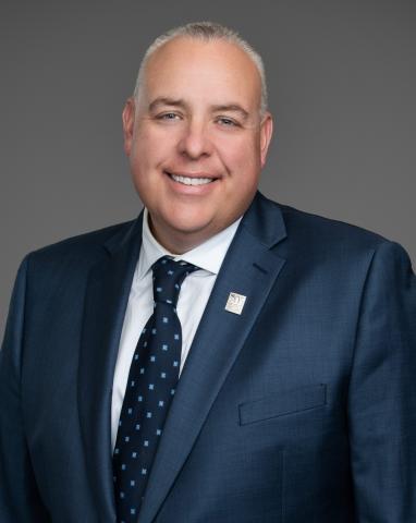 Councillor Steve Darling headshot. There is a smiling man in a dark blue suit and tie. The is background behind the councillor is grey.