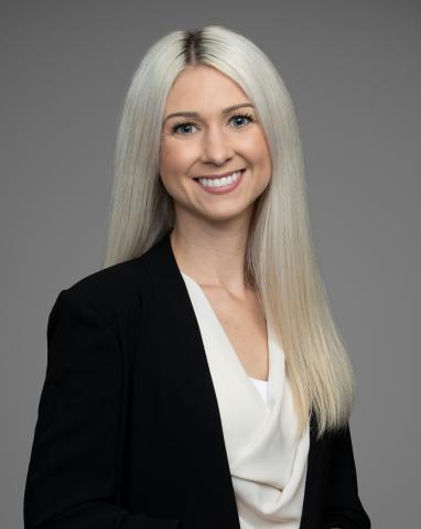 Headshot of Councillor Paige Petriw. There is a smiling woman with auburn-coloured hair. The background behind the councillor is grey.