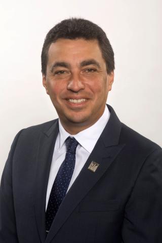 Headshot of Councillor Dean Washington. There is a smiling man wearing a black suit and tie. The background behind the councillor is light grey.