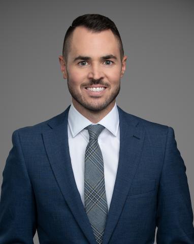 Headshot of Mayor Brad West. There is a smiling man in a suit and tie. The background behind the mayor is grey.