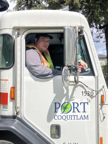 Solid waste collector driving a truck with the Port Coquitlam city logo on the door.