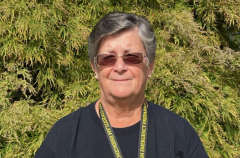 A photo of a woman wearing sunglasses standing outside in the sun on front of a tree