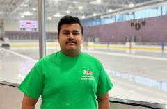 A man in a green shirt standing in front of an ice rink