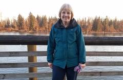 A woman wearing a winter jacket on a boardwalk with a lake and trees in the distance