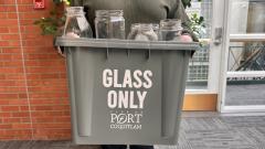 Person holding up grey glass recycling bin inside with glass jars inside
