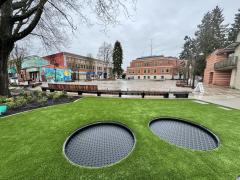 Photo of Leigh Square with green grass, two in-ground trampolines, open concept space with City Hall in background