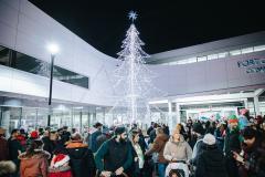 lit up outdoor christmas tree with crowd surrounding outside community centre