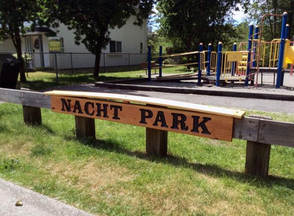 Nacht Park signage. The sign is wooden with dark lettering. The sign is on a wooden barrier.
