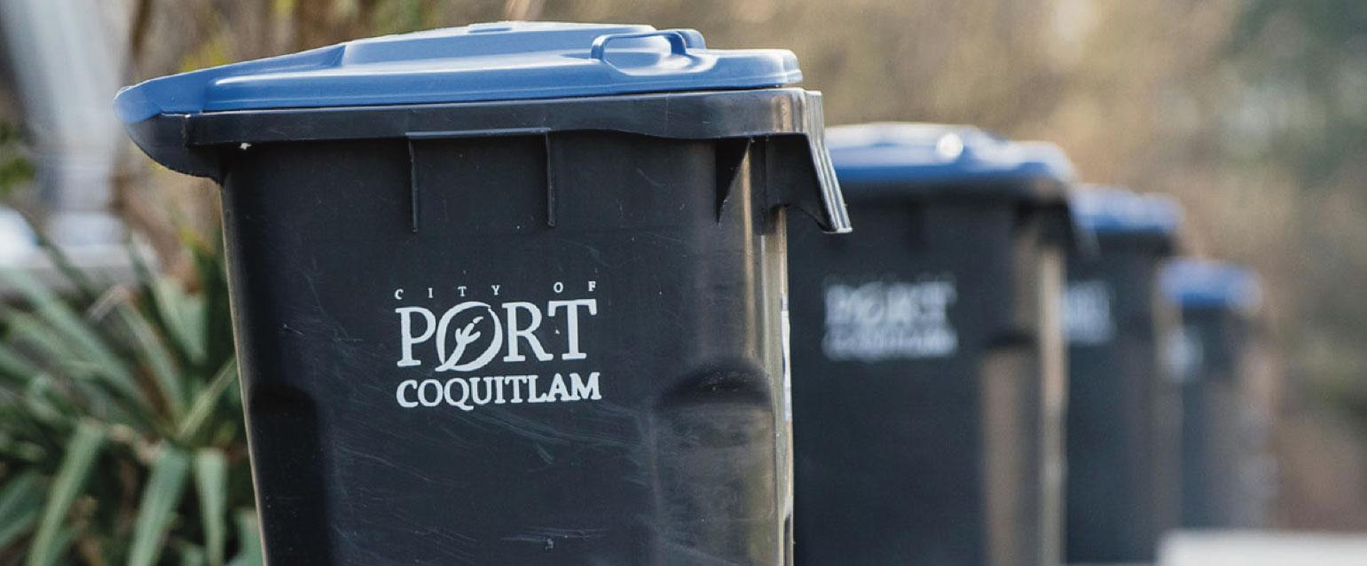 Lined up garbage cans on a street that say 'City of Port Coquitlam'