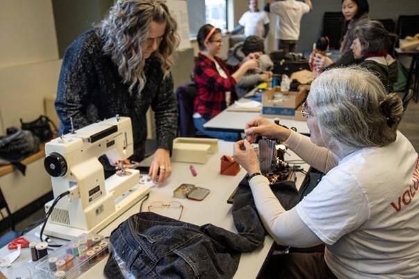 A woman helping someone repair somethign with a sewing machine