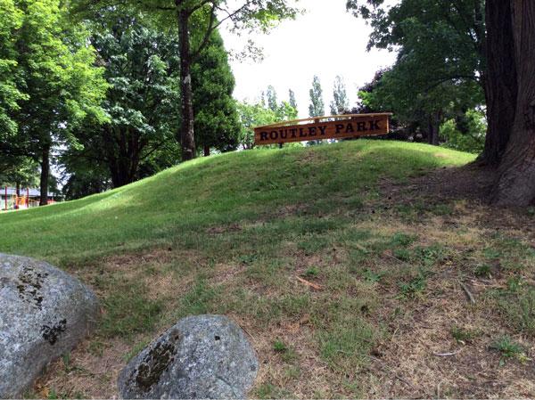 Routley Park sign. The sign is wooden with dark lettering sitting at the top of a hill.
