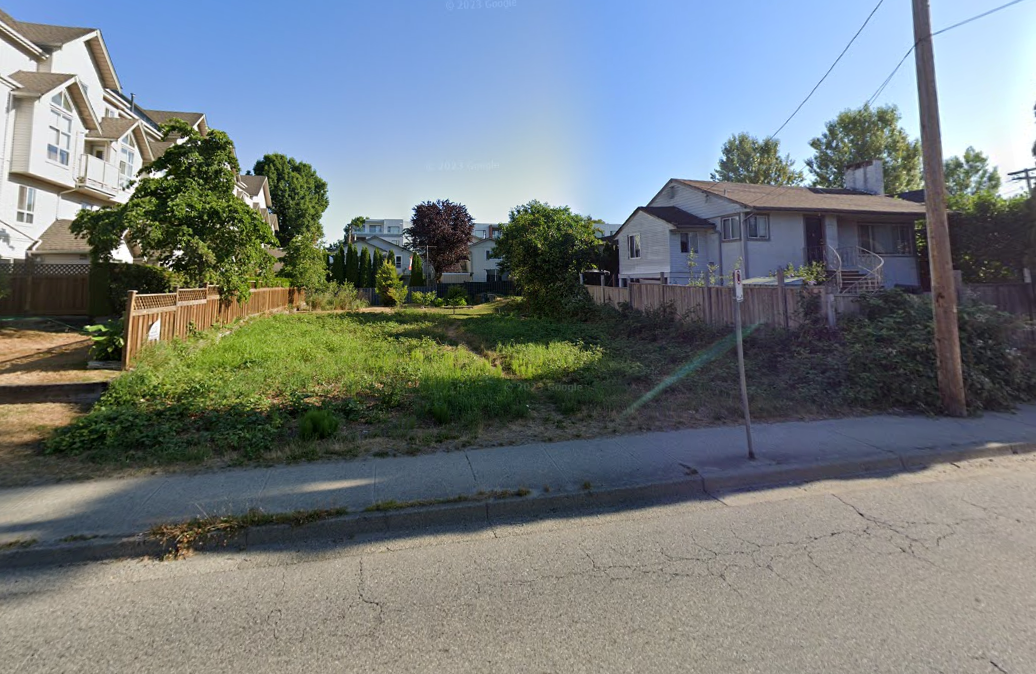 Empty lot lush with tall, green grass. The lot is surrounded by fences from adjacent properties.