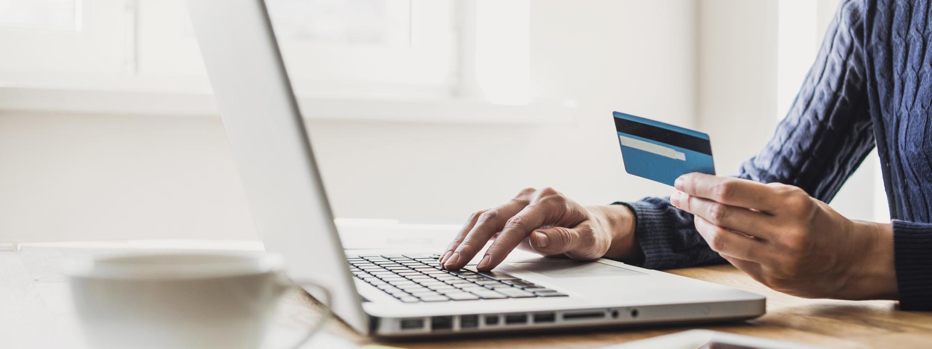 Person holding a credit card while typing on a laptop to make an online payment