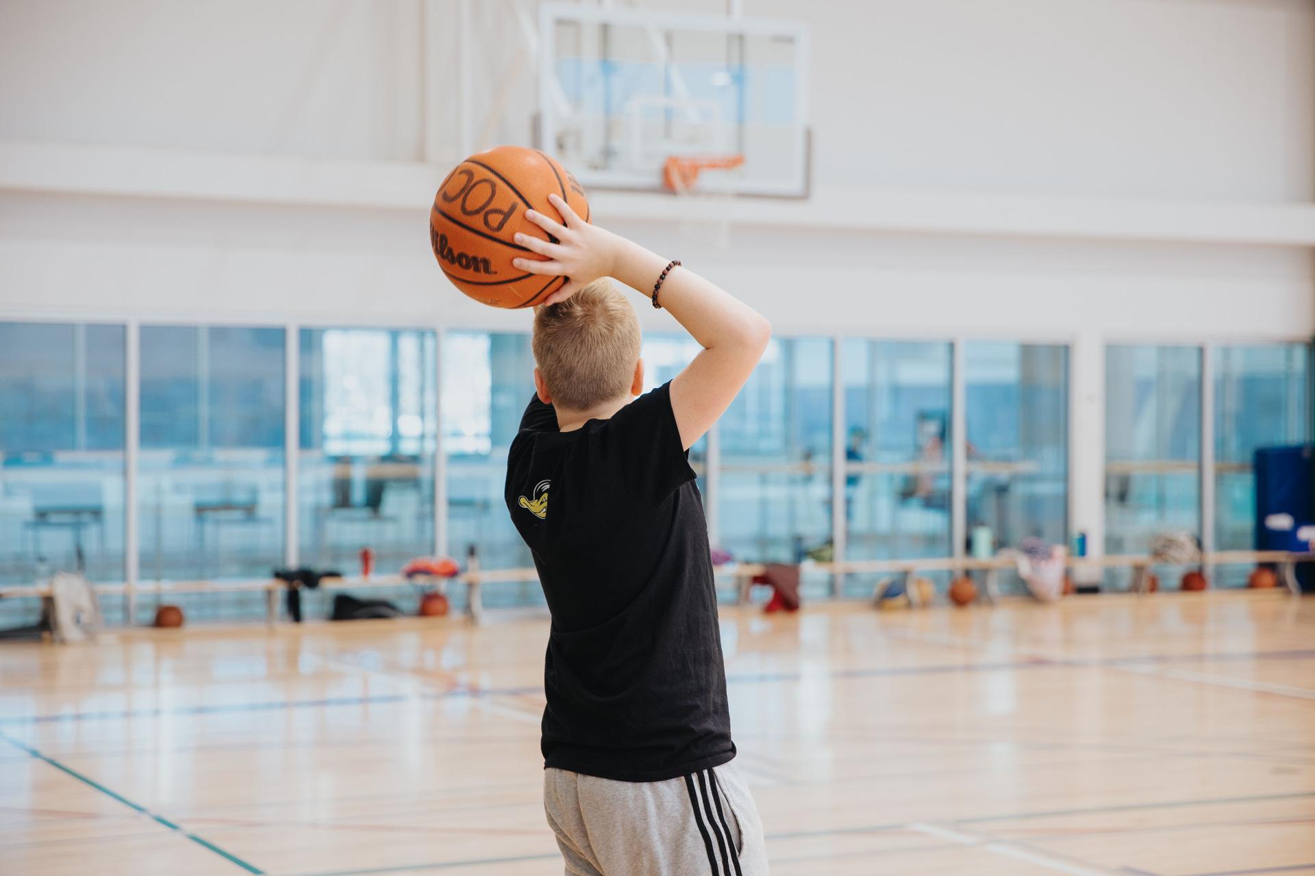 Youth shooting a basketball inside rec centre gymnasium