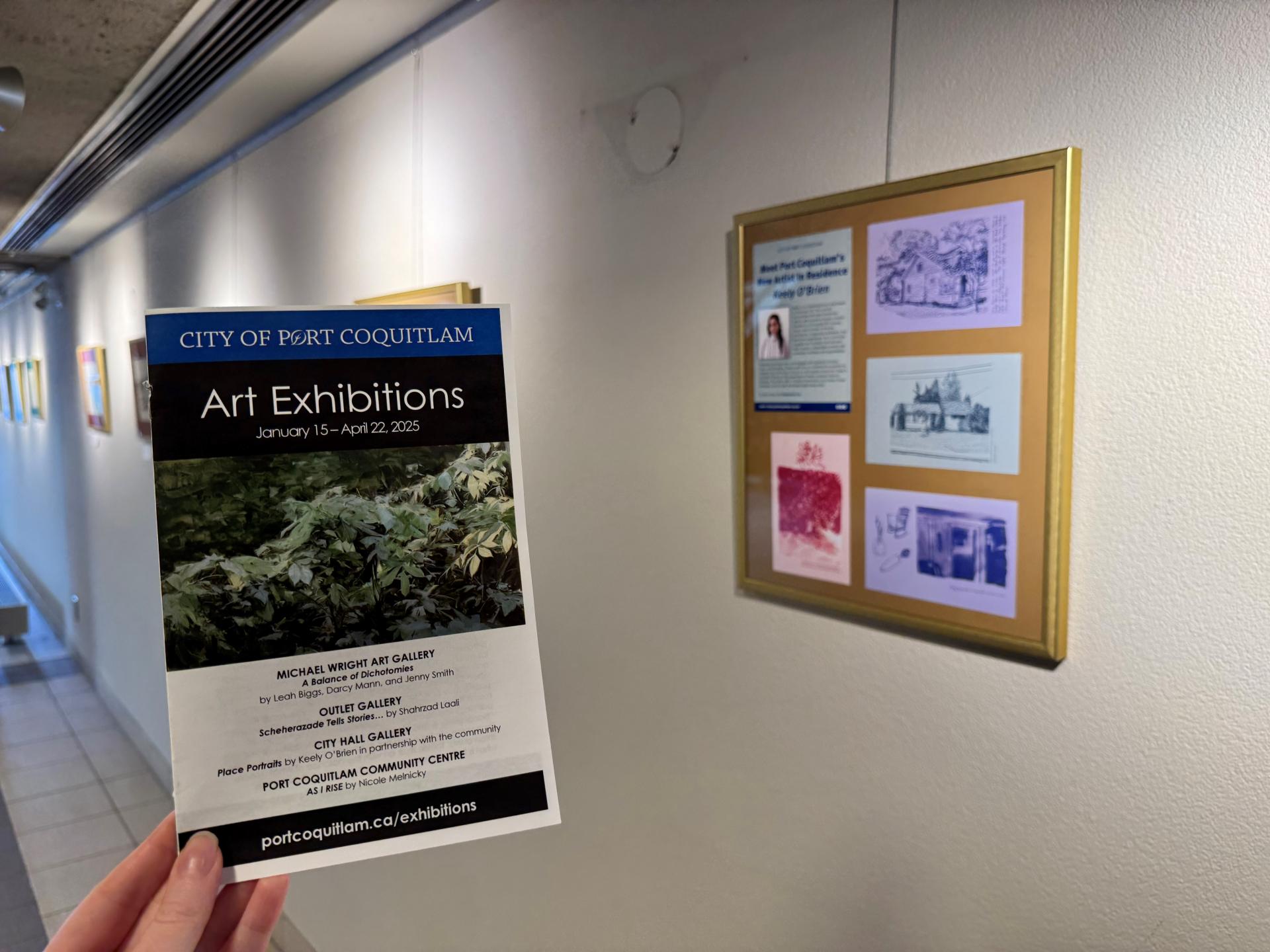 Holding a brochure for art exhibitions in front of a wall of artwork on display