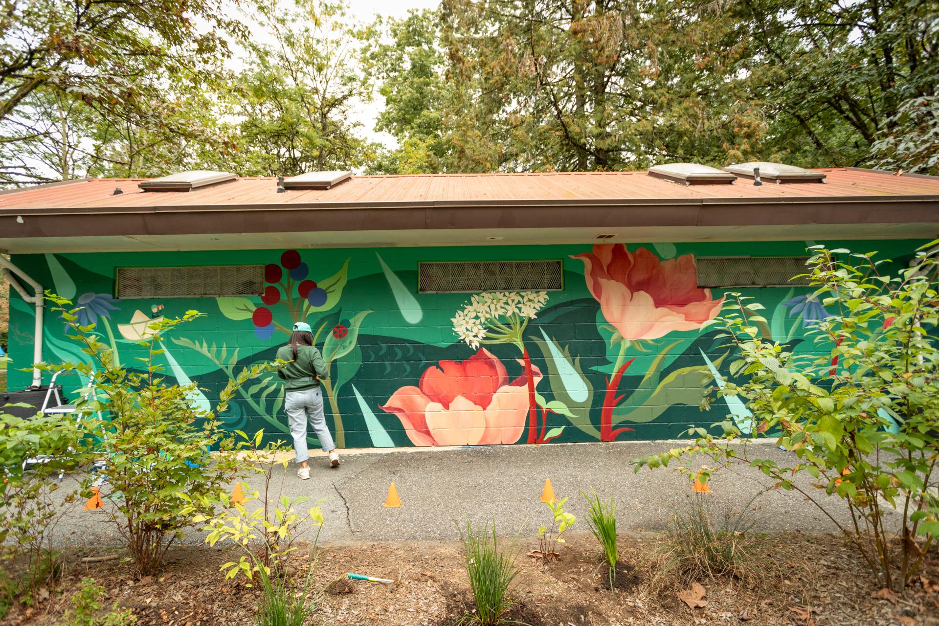 Person standing in front of floral art mural on building at Lions Park