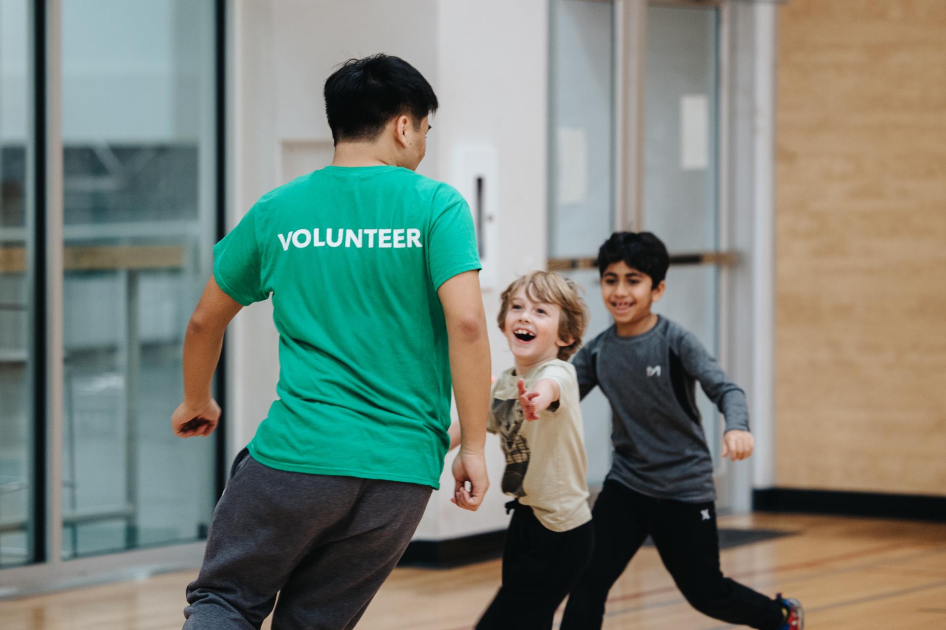 volunteer running with kids in gymnasium sports program